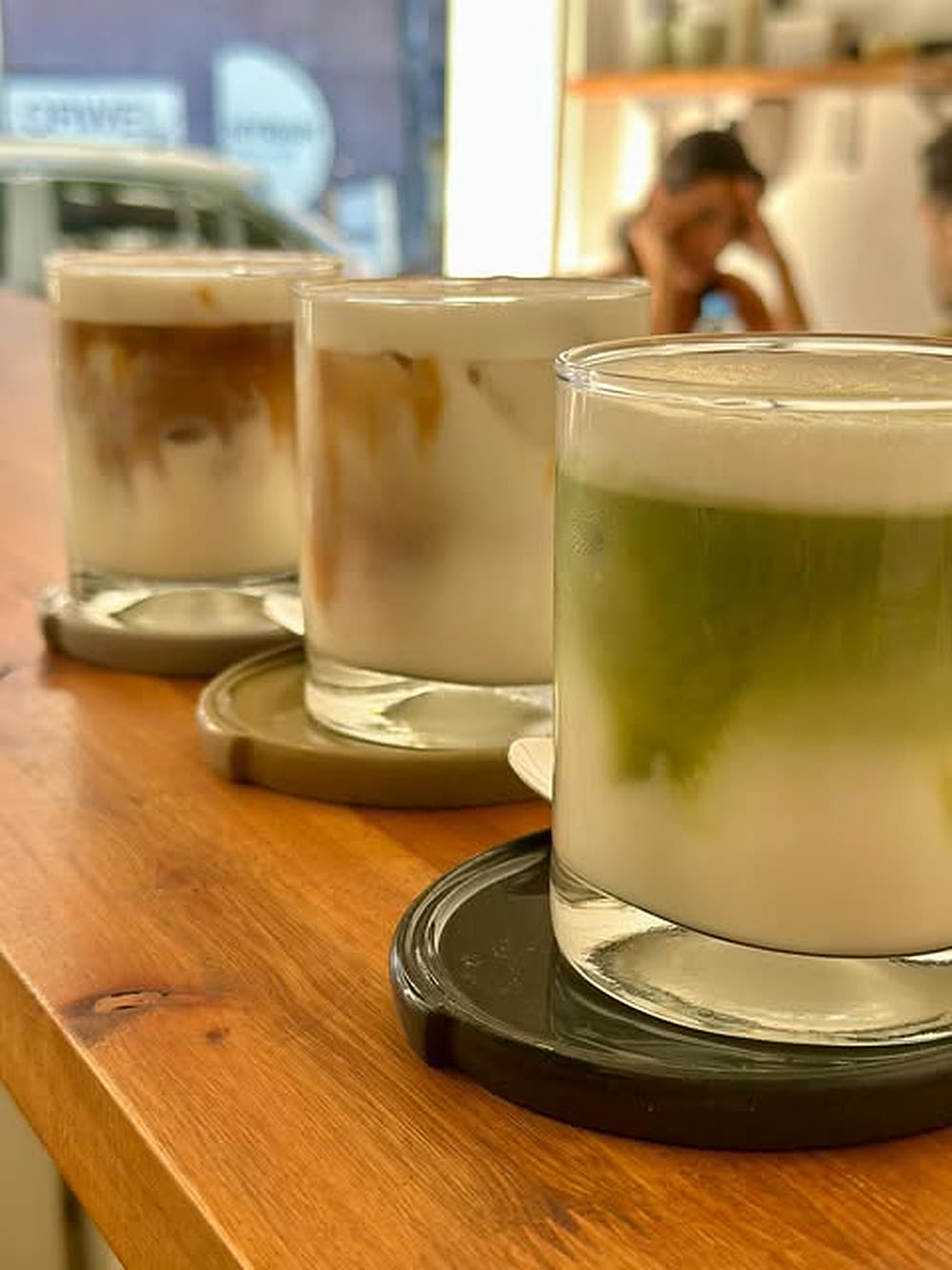 Cold brew, iced latte y matcha latte de Demente alineados sobre la barra de madera